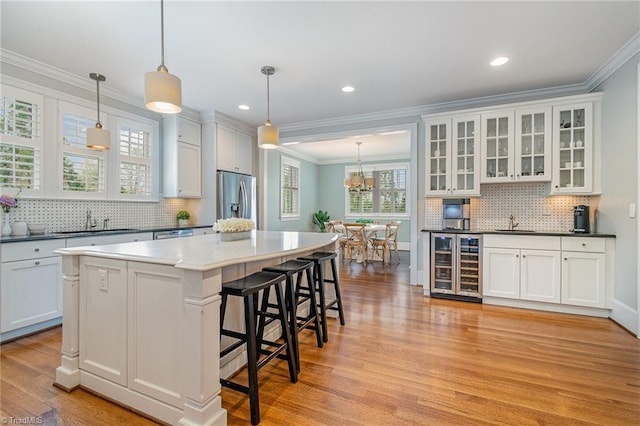 kitchen featuring ornamental molding, a sink, wine cooler, stainless steel fridge with ice dispenser, and light wood finished floors