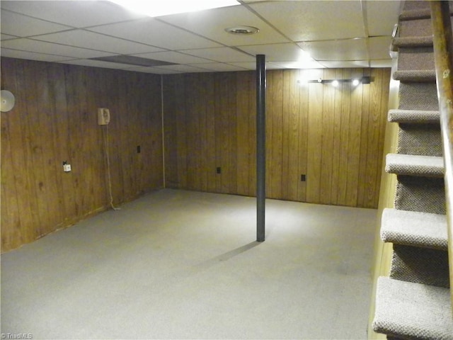 basement featuring a paneled ceiling, wooden walls, and light colored carpet