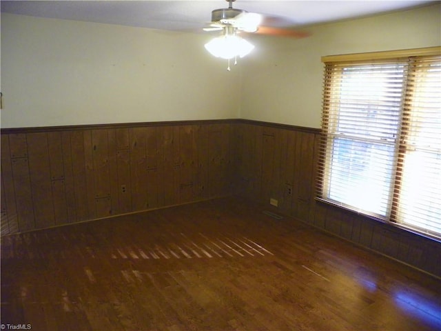 empty room featuring dark hardwood / wood-style floors, wooden walls, and ceiling fan