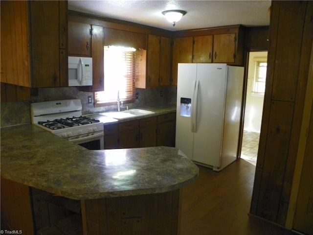 kitchen featuring kitchen peninsula, tasteful backsplash, dark hardwood / wood-style flooring, sink, and white appliances