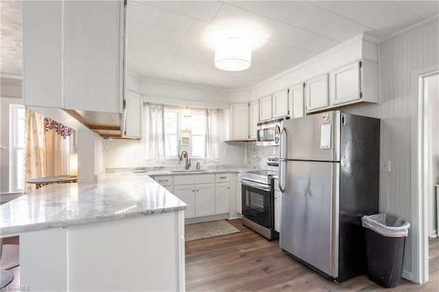 kitchen with crown molding, appliances with stainless steel finishes, white cabinetry, a sink, and a peninsula