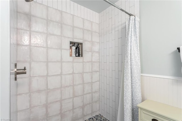 bathroom with a wainscoted wall and a tile shower