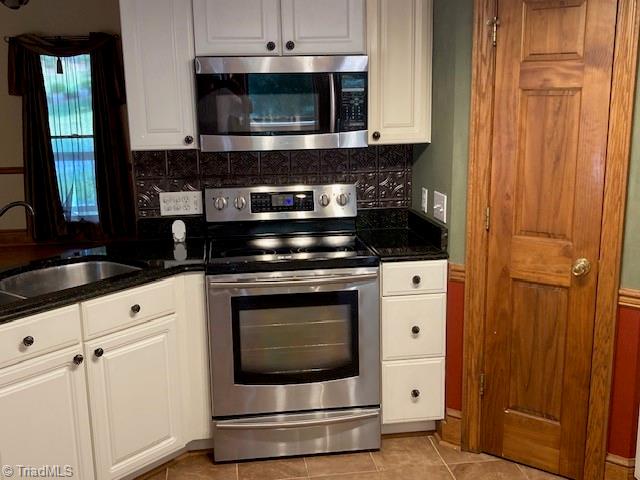 kitchen featuring light tile patterned floors, appliances with stainless steel finishes, sink, decorative backsplash, and white cabinets