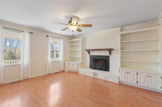 unfurnished living room featuring ceiling fan, built in features, light hardwood / wood-style floors, and a brick fireplace