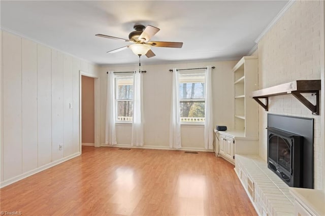 unfurnished living room with ceiling fan, a fireplace, light hardwood / wood-style floors, and ornamental molding