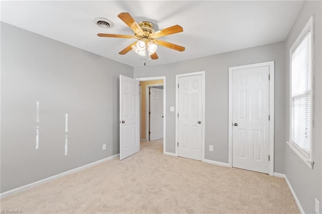 unfurnished bedroom with ceiling fan, light carpet, and two closets