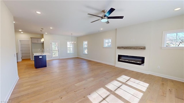 unfurnished living room with recessed lighting, a healthy amount of sunlight, a glass covered fireplace, and light wood finished floors