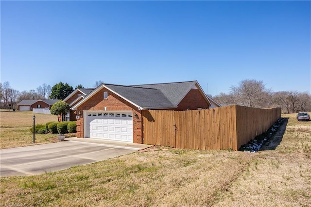 view of home's exterior featuring driveway, fence, a yard, an attached garage, and brick siding