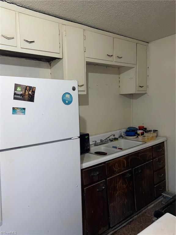 kitchen featuring sink, white cabinets, a textured ceiling, and white fridge