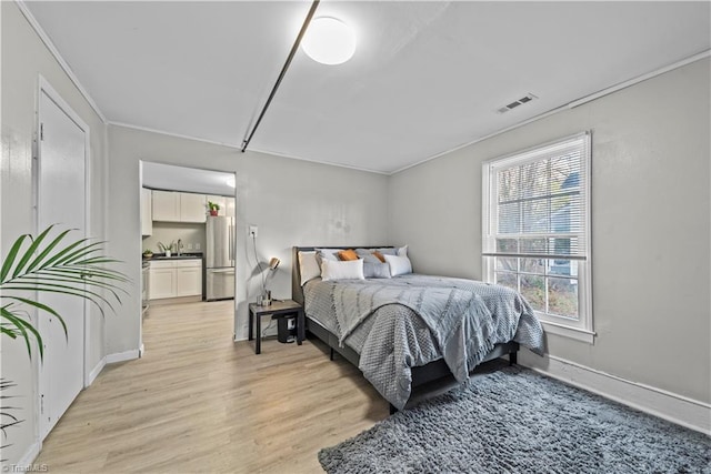 bedroom featuring stainless steel refrigerator, sink, and light wood-type flooring