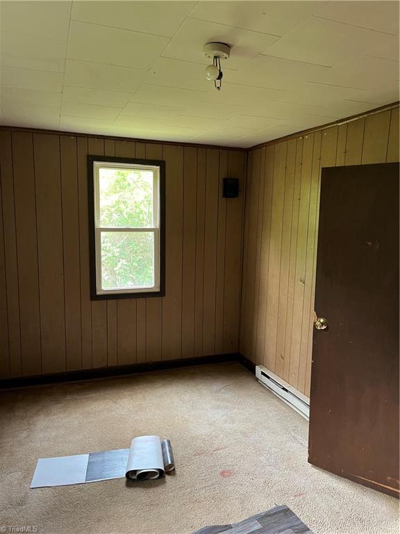 empty room with a baseboard radiator, light carpet, and wood walls