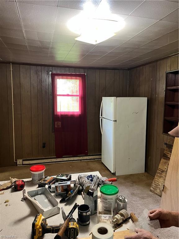 kitchen with freestanding refrigerator, wood walls, dark brown cabinetry, light countertops, and carpet floors