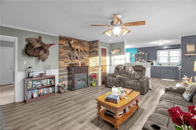 living room featuring crown molding, a stone fireplace, hardwood / wood-style floors, and a textured ceiling