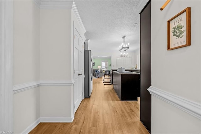 corridor featuring a notable chandelier, light wood-style floors, baseboards, and a textured ceiling