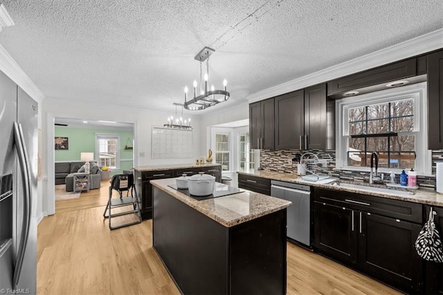 kitchen with a kitchen island, a chandelier, light wood-style flooring, appliances with stainless steel finishes, and a sink