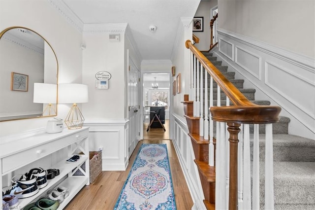 hall with stairway, ornamental molding, an inviting chandelier, light wood-style floors, and a decorative wall