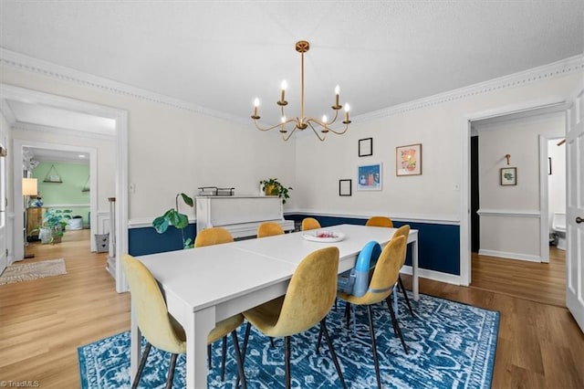 dining area with light wood-style flooring, baseboards, crown molding, and an inviting chandelier