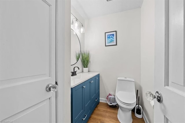 half bath featuring vanity, toilet, wood finished floors, and baseboards