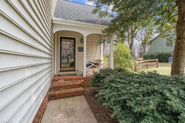 view of exterior entry with a porch and a shingled roof