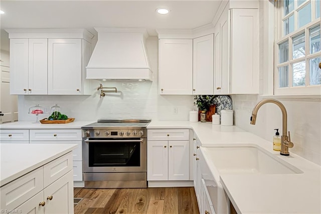 kitchen with custom exhaust hood, white cabinetry, and stainless steel stove