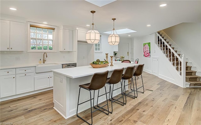 kitchen featuring sink, a center island, white cabinetry, light hardwood / wood-style floors, and a skylight