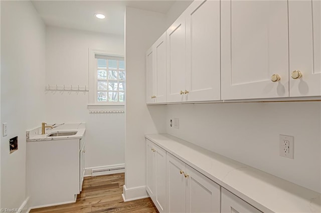 clothes washing area with light hardwood / wood-style floors, sink, and baseboard heating