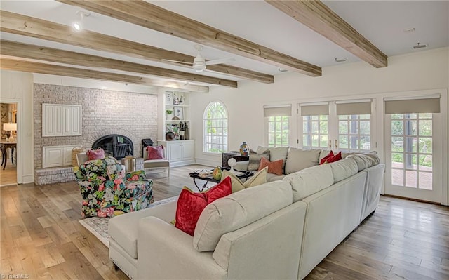 living room featuring beamed ceiling, a fireplace, light hardwood / wood-style floors, and ceiling fan