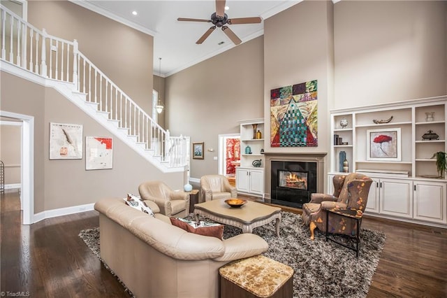 living room featuring dark wood finished floors, stairway, ornamental molding, a towering ceiling, and a glass covered fireplace