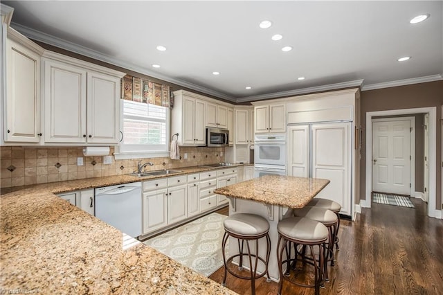 kitchen with light stone counters, white dishwasher, ornamental molding, a sink, and stainless steel microwave