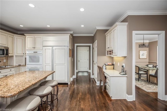 kitchen featuring a kitchen bar, stainless steel microwave, dark wood finished floors, black electric cooktop, and white double oven