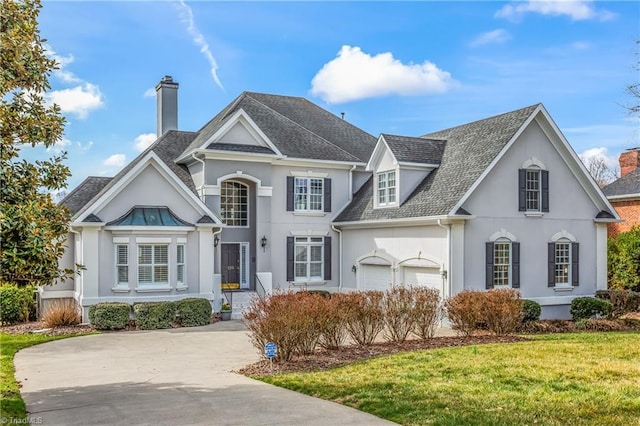 view of front of home featuring a front lawn, stucco siding, a chimney, a garage, and driveway