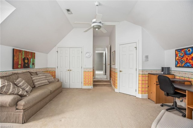 office area featuring a ceiling fan, a wainscoted wall, visible vents, lofted ceiling, and light colored carpet