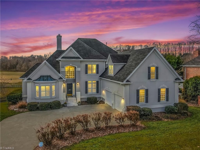 view of front of house featuring a shingled roof, stucco siding, a chimney, driveway, and an attached garage