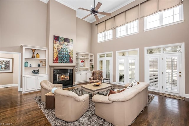 living area with a glass covered fireplace, crown molding, a high ceiling, and dark wood-style flooring