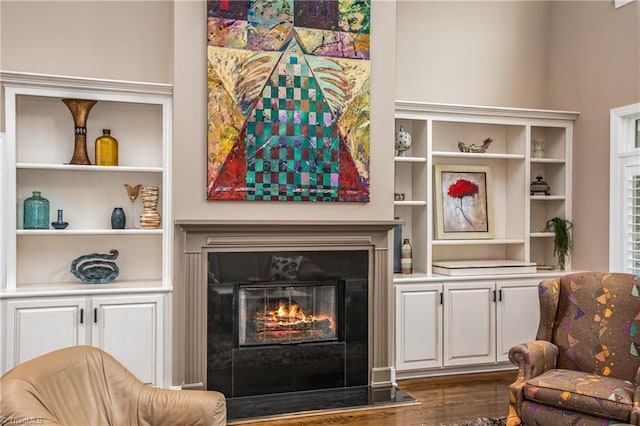 living area with a glass covered fireplace, dark wood-type flooring, and built in shelves