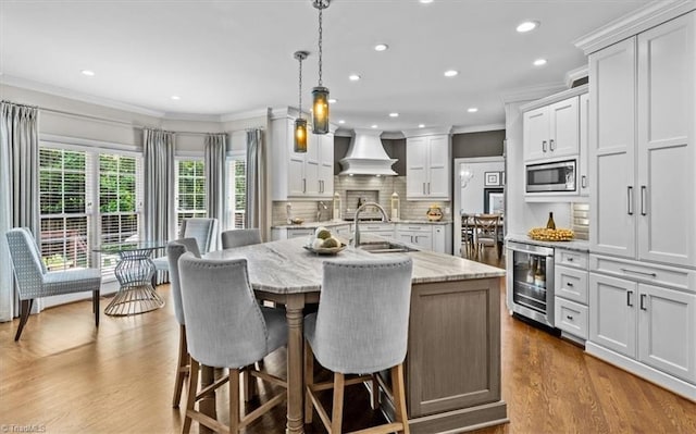 1905 Regents Park Ln, Greensboro, NC 27455 - kitchen featuring wine cooler, custom exhaust hood, crown molding, stainless steel microwave, and an island with sink