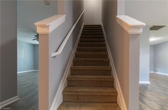 stairs featuring wood finished floors, baseboards, and a ceiling fan