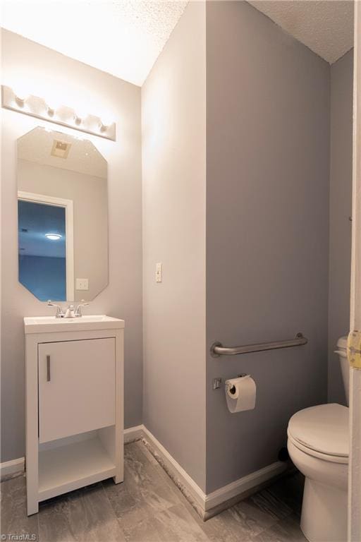 bathroom featuring toilet, vanity, baseboards, and a textured ceiling