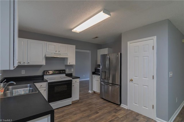 kitchen with stainless steel fridge, electric range oven, a sink, dark countertops, and under cabinet range hood