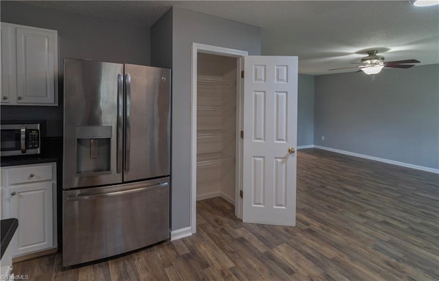 kitchen with appliances with stainless steel finishes, white cabinets, a ceiling fan, dark wood finished floors, and baseboards