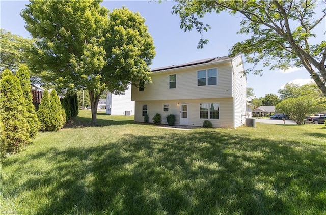 rear view of property with central AC, a lawn, and solar panels
