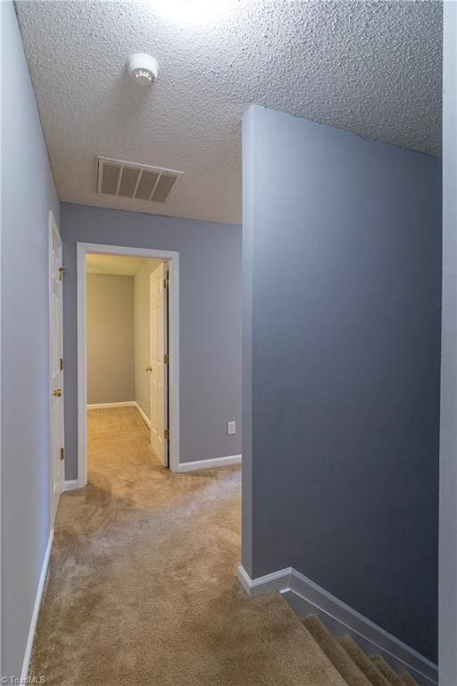hall featuring a textured ceiling, carpet flooring, and baseboards