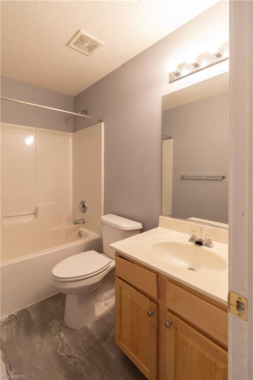 full bathroom with toilet, vanity, a textured ceiling, and tub / shower combination