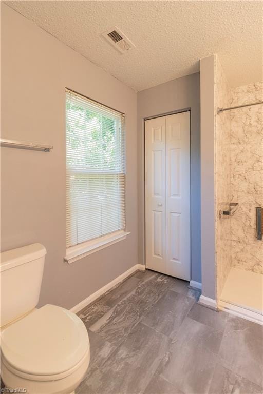 bathroom with a shower stall, a textured ceiling, baseboards, and toilet