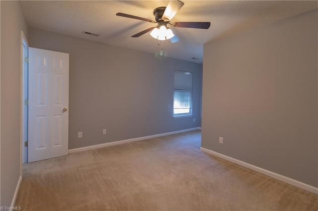 spare room featuring light carpet, ceiling fan, a textured ceiling, and baseboards