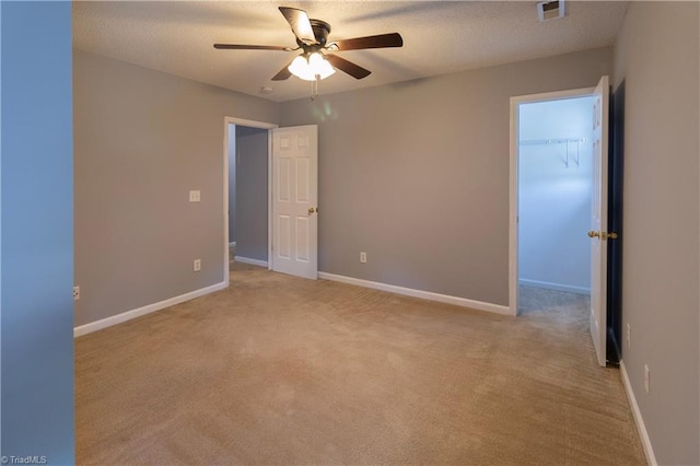 unfurnished bedroom with light carpet, a walk in closet, baseboards, ceiling fan, and a textured ceiling