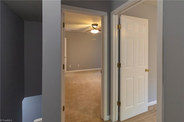 hall with light carpet, baseboards, and a textured ceiling