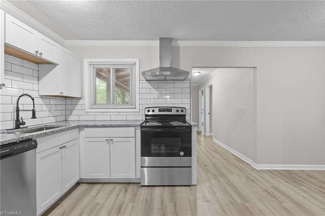 kitchen with stainless steel appliances, wall chimney exhaust hood, light wood-style floors, and ornamental molding