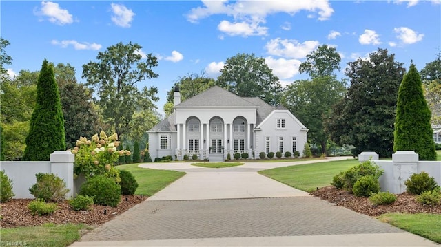 view of front of home with driveway, a fenced front yard, a chimney, and a front lawn