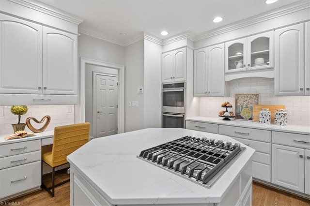 kitchen featuring stainless steel appliances, a kitchen island, white cabinetry, light wood-type flooring, and light stone countertops